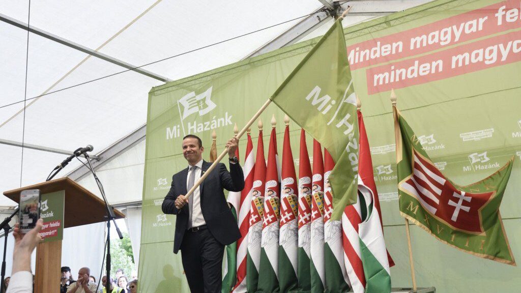 Laszlo Torokai waving green flag of Our Homeland movement on stage in front of Hungarian flags