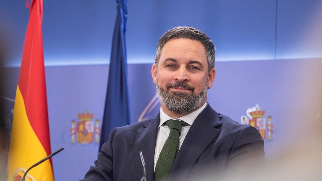 VOX leader Santiago Abascal at podium in focus, unfocused onlookers at sides in front