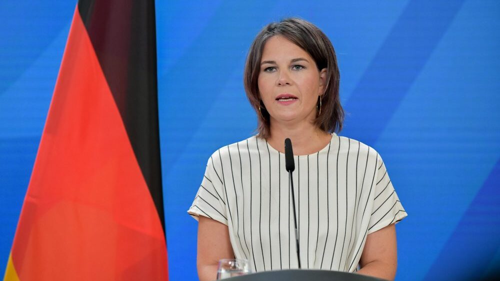 Annalena Baerbock behind podium blue backdrop German flag to the left