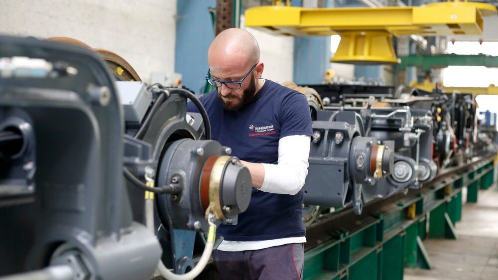 Man in factory by machine looking focused at what his hands are doing