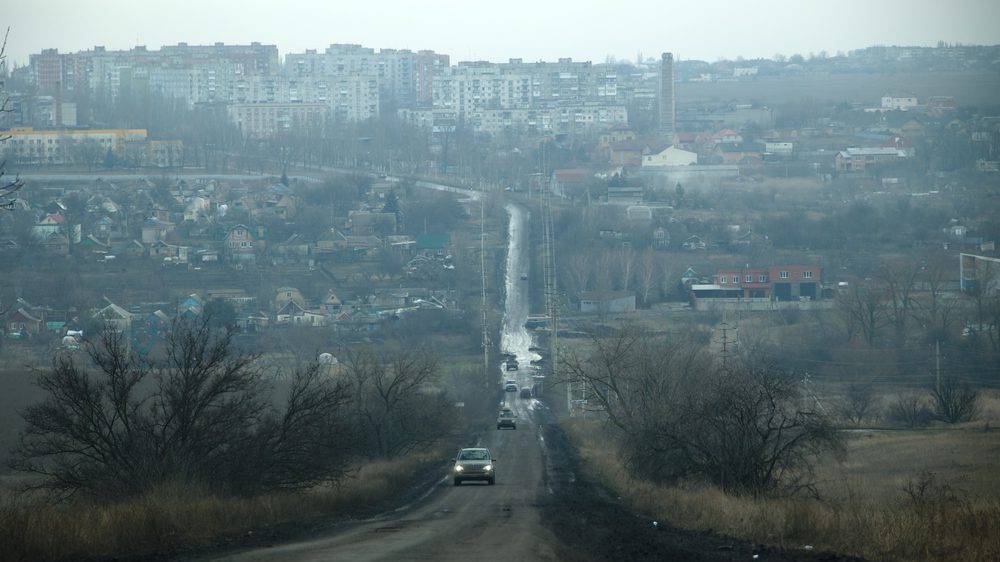 Straight road down hill and up towards city of Bakhmut, a few vehicles