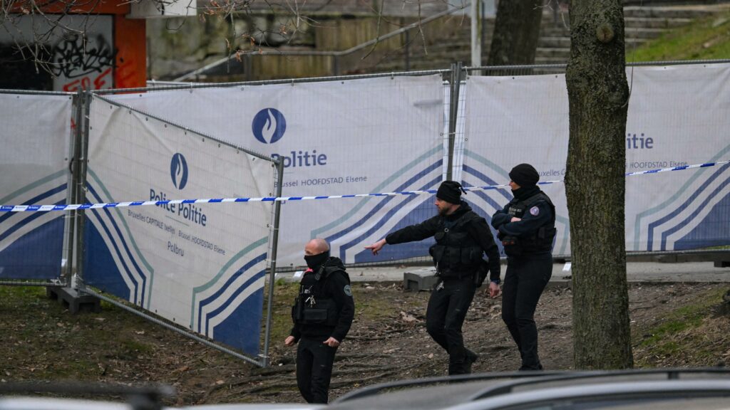 Police officers walk near a police fence blocking off an investigation area at the "Cite du Peterbos" neighbourhood, where a man was killed overnight in a new shooting linked to drug trafficking in the municipality of Anderlecht, Brussels, on February 7, 2025.