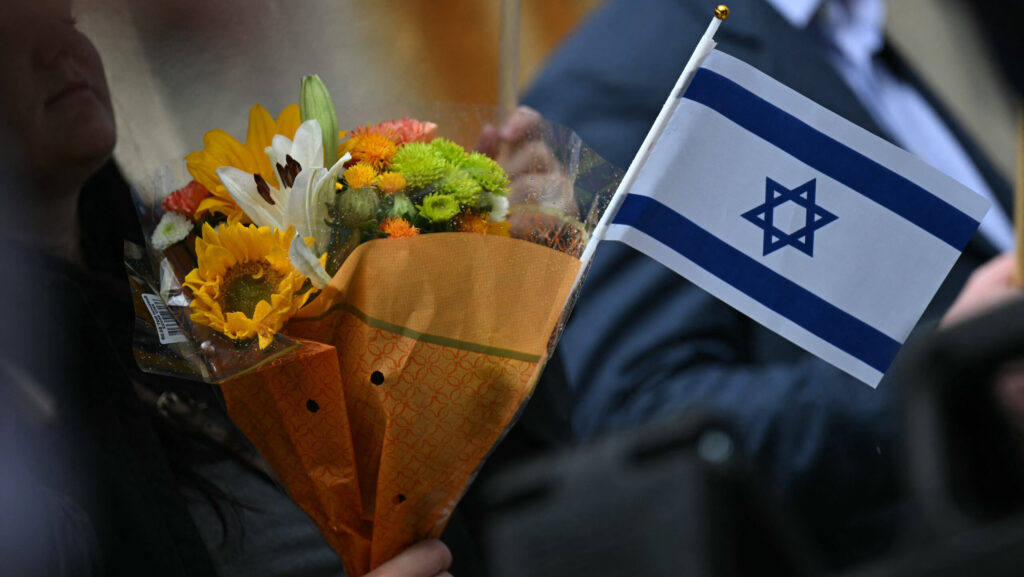 A woman holds flowers and an Israeli national flag in a sign of support outside the Capital Jewish Museum following the shooting of Israeli embassy staffers, Yaron Lischinsky and Sarah Lynn Milgrim by a gunman who shouted "free Palestine."