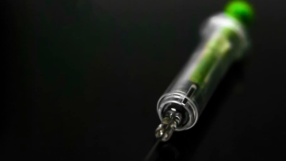 injection needle with green content looking toxic against black background