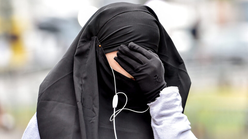A Muslim woman wearing a long sleeved top, black gloves and a head scarf covers her face along a street in the northern French city of Lille.