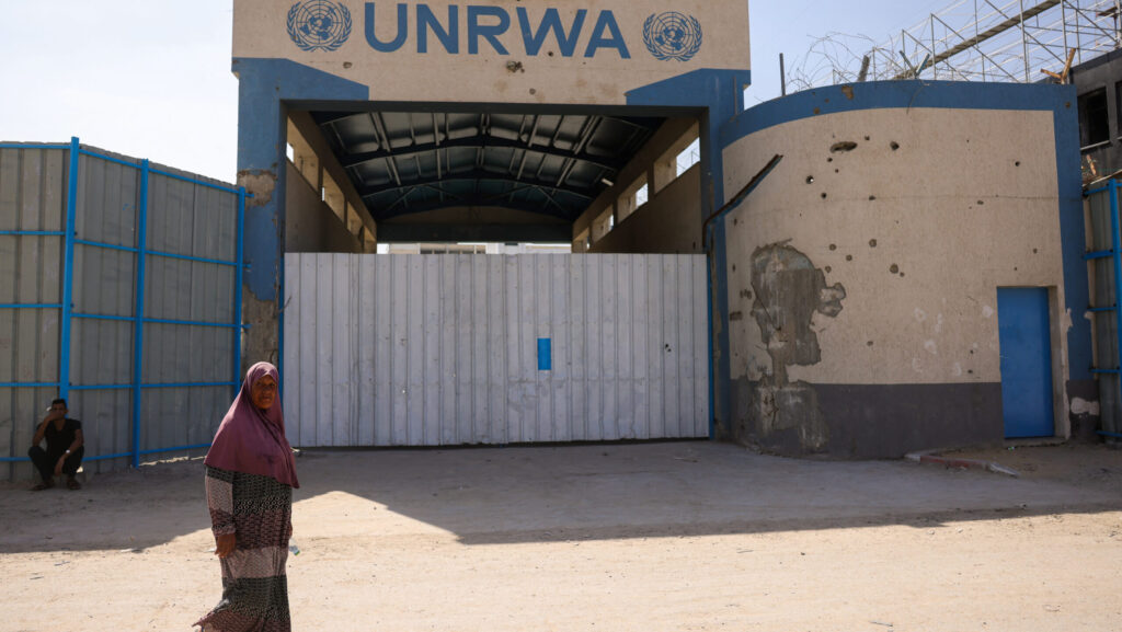 Woman in Muslim garb walks by boarded up HQ for UNRWA in Gaza City