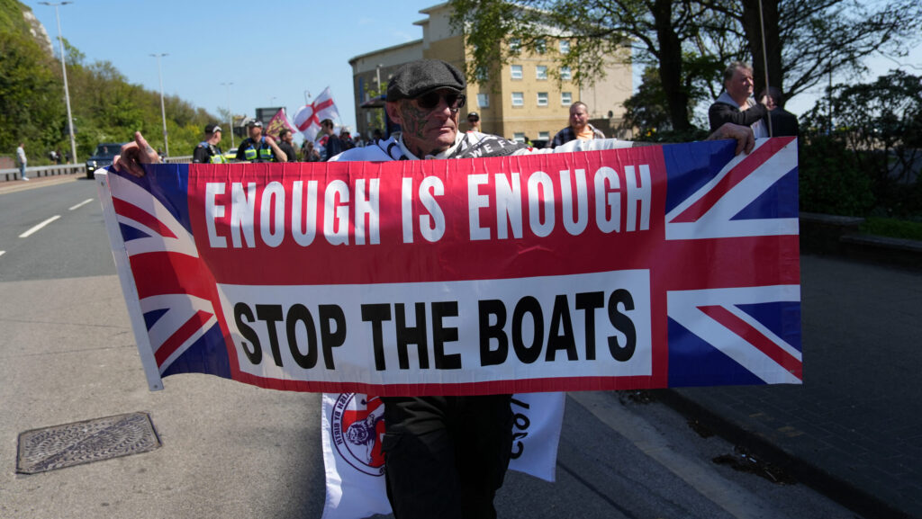 Protester against uncontrolled illegal immigration carrying banner with text "enough is enough, stop the boats"