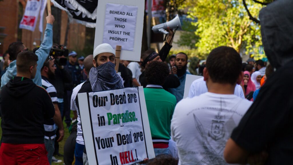 Muslim protesters carry signs reading "Behead all those who insult the Prophet" and "Our dead are in Paradise. Your dead are in HELL!"