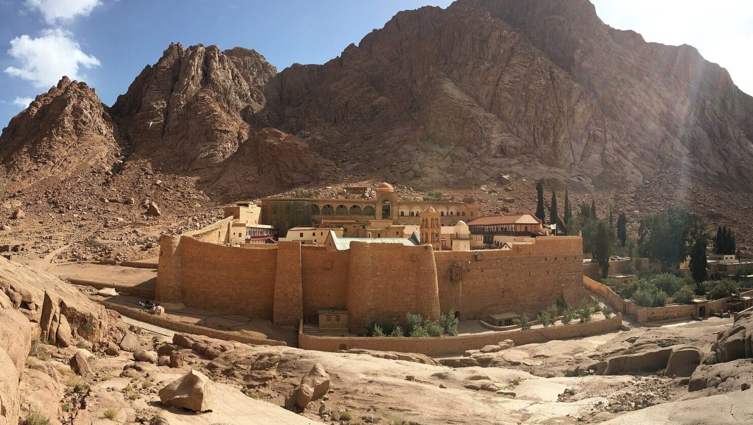 Buildings contained within a wall at the foot of a mountain in desert landscape