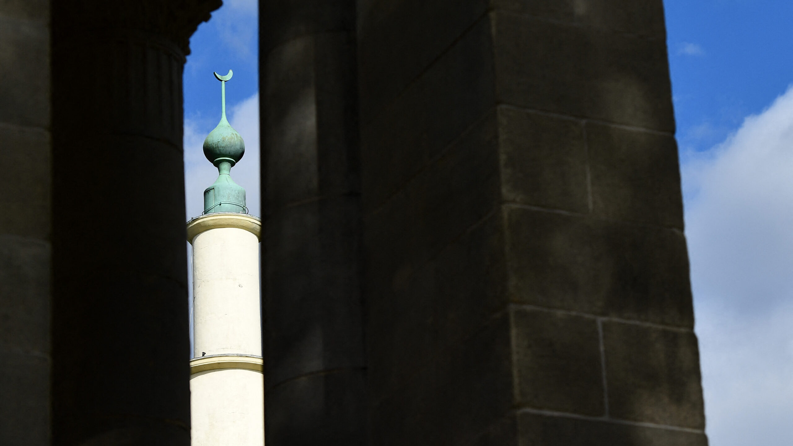Top of minaret of Brussels great mosque seen in sunlight in gap between two dark pillars