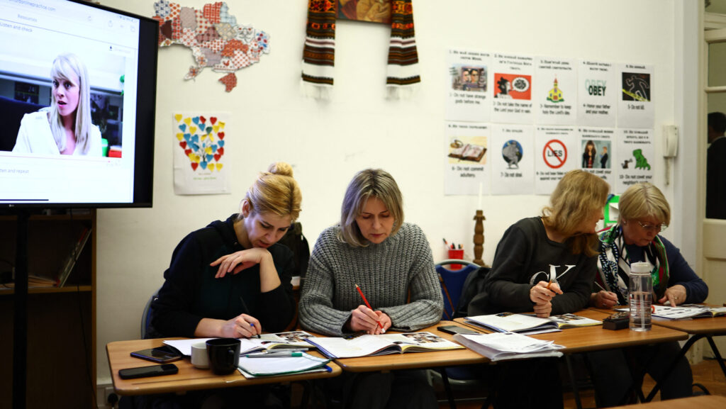 Four women seated at desks with books and notebooks in front of them