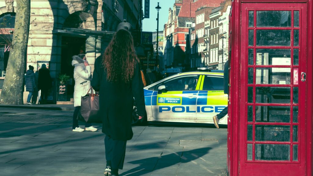 Woman seen from behind walking towards a Metropolitan Police car in London and passing by a red phone booth on her right