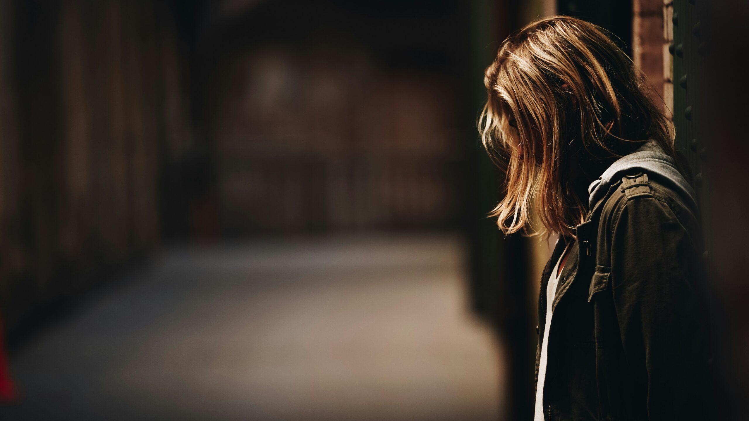 Girl leans agaisnt wall in dark hallway (sexual assault illustration) Unsplash