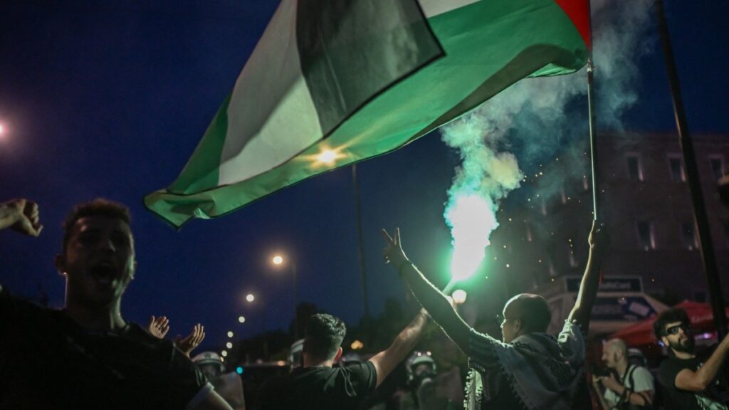 Protesters burn a flare and wave a Palestinian flag outside the Greek Parliament during a demonstration in Athens on June 15, 2025.