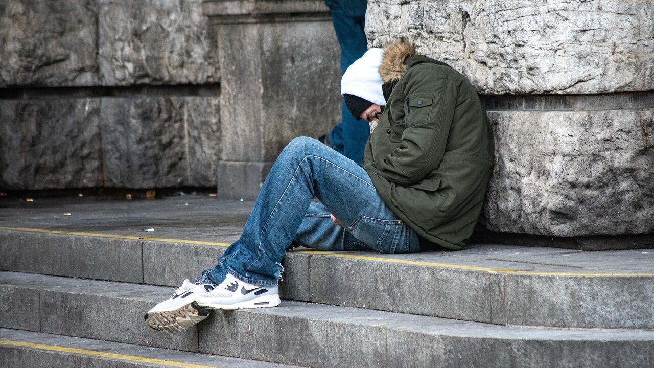 Young homeless man sleeping on steps of stone building