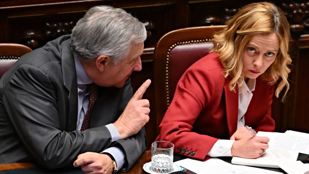 Antonio Tajani holding one finger up looking at Giorgia Meloni who looks irritated and looks toward camera