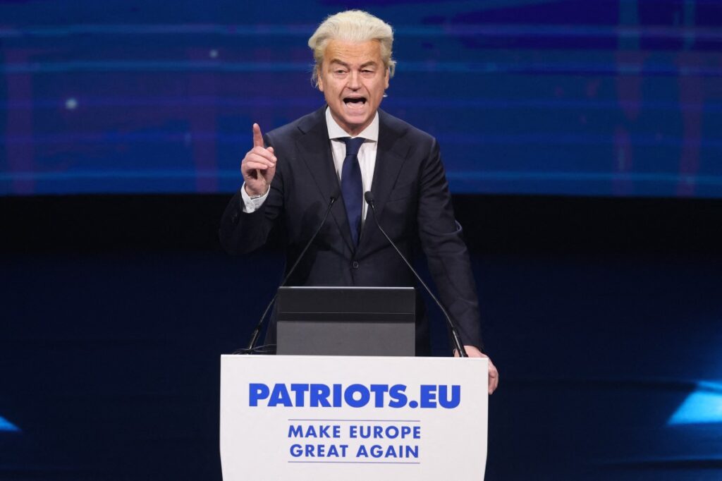 Wilders speaking at Patriots summit standing behind podium pointing upward with right index finger