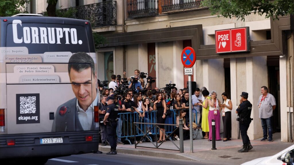 Bus parked outside PSOE offices with image of Sánchez and the word "Corrupt"