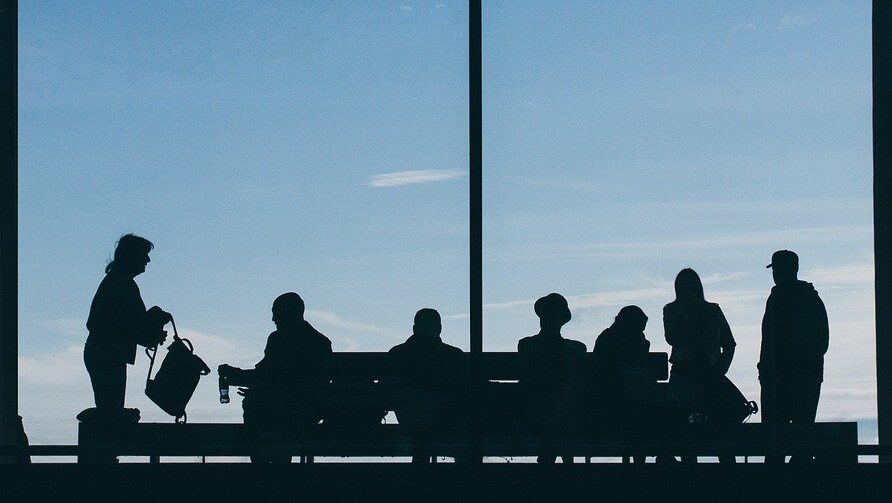 silhouette of people seated & standing against window waiting at airport