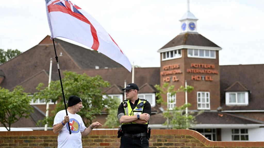 A protester wearing waves a mixed Union Jack and St. George’s flag while speaking to a police officer during an ‘Enough is Enough’ demonstration in Aldershot on August 4, 2024.