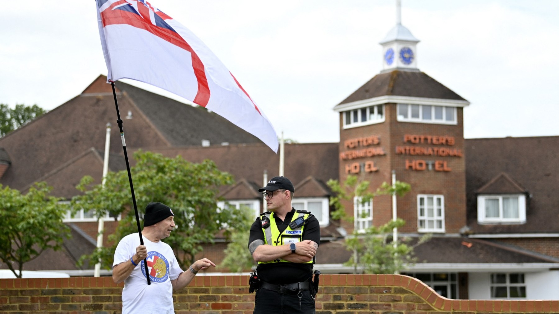 A protester wearing waves a mixed Union Jack and St. George’s flag while speaking to a police officer during an ‘Enough is Enough’ demonstration in Aldershot on August 4, 2024.