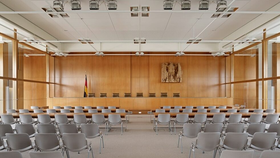 empty court chambers with gray plastic chairs and carpet, blond wood walls and desks and 8 empty leather chairs for the judges