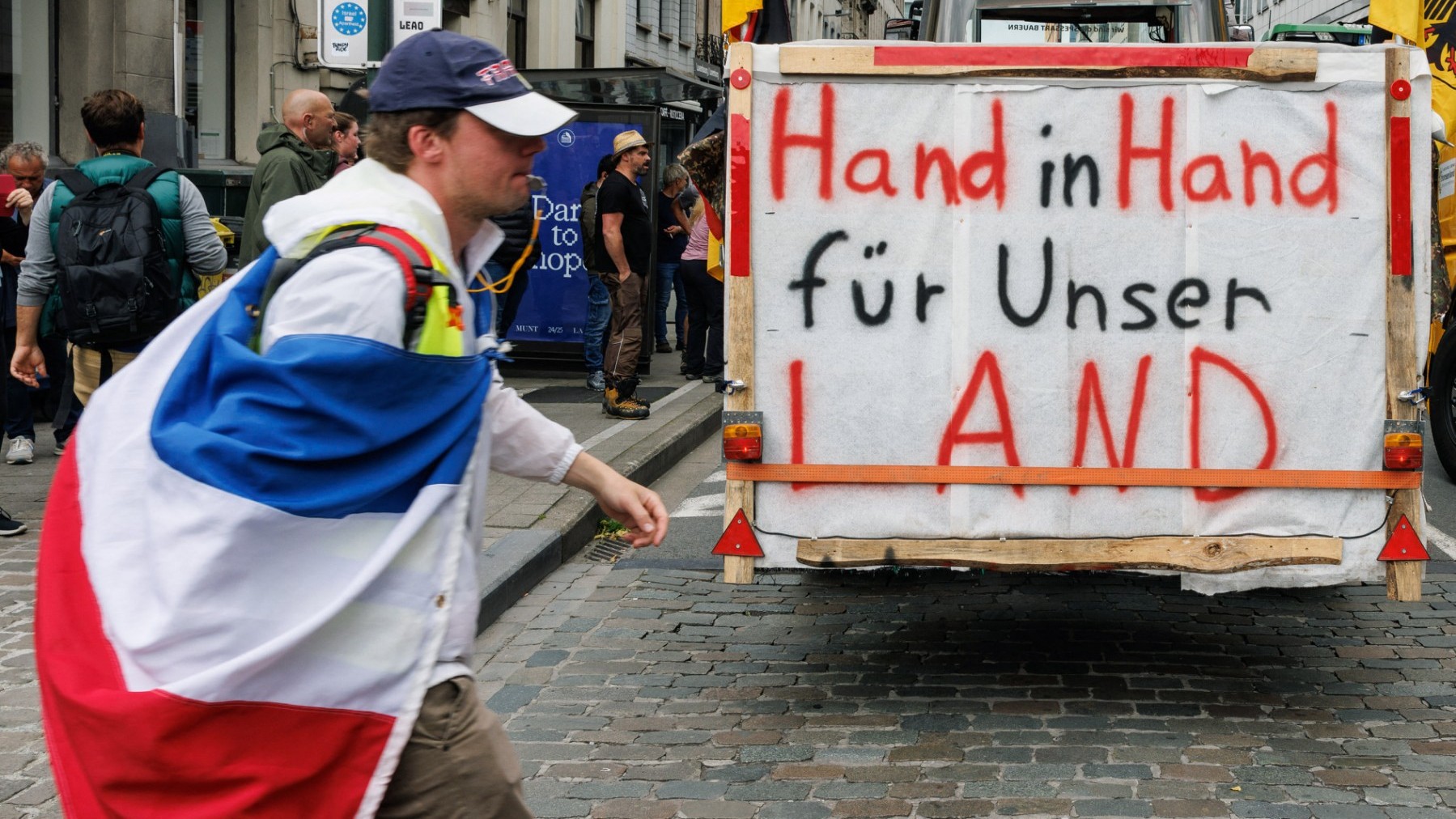 A demonstrator wrapped in a Dutch national flag walks past a tractor with a placard reading ’Hand in hand for our country’ at the European Parliament Building during a protest against EU regulations in Brussels on June 4, 2024.