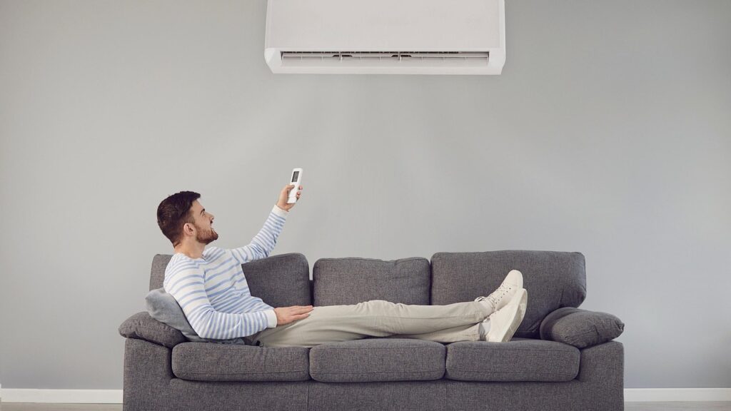 man sitting comfortably on couch turning on air conditioning unit with remote control