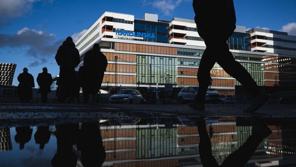Building of Karolinska University Hospital in Stockholm reflecting in wet pavement, outline of people walking