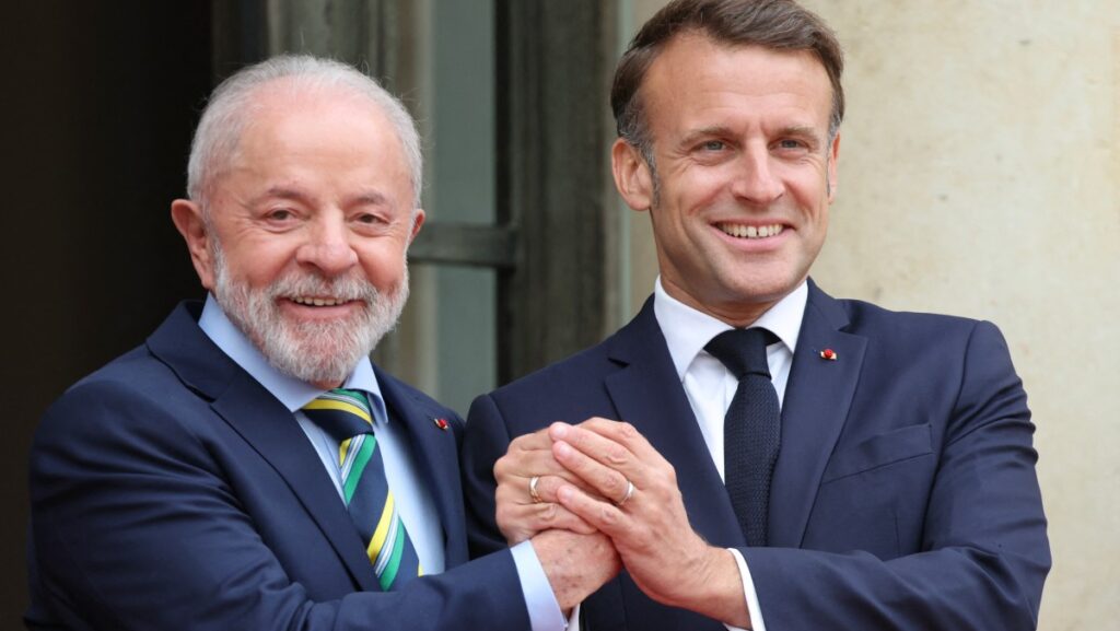 Lula and Macron clasping hands and smiling.