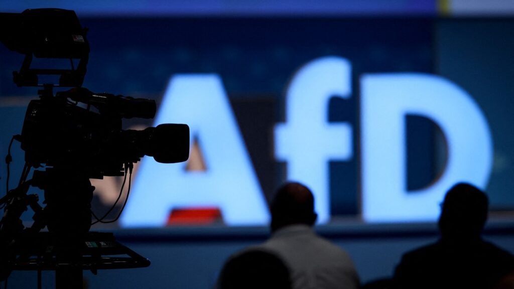 A blurred AfD logo with a video camera in the foreground