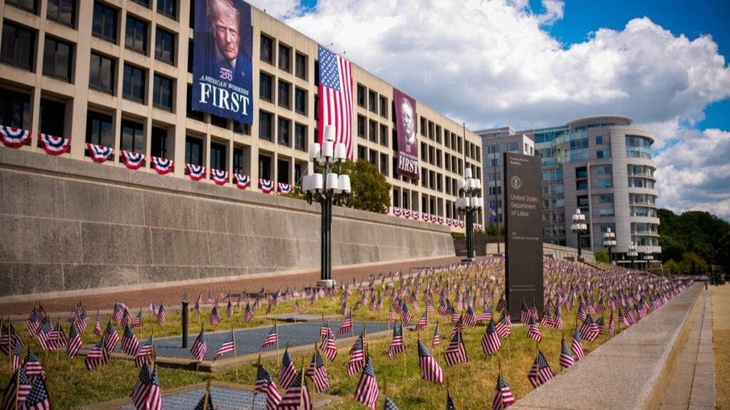 Hundreds of small American flags on the lawn of and a photo of U.S. President Donald Trump on the facade of the U.S. Department of Labor building seen on August 29, 2025 in Washington, D.C.