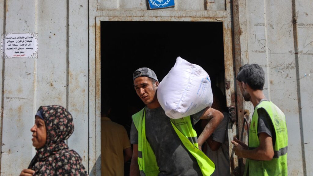 man carrying sack of food supplies on his shoulder coming out of doorway