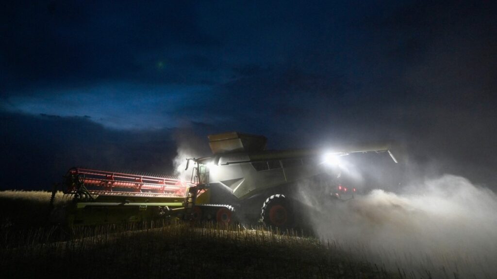 A French farmer drives his tracked combine harvester while harvesting a field of rapeseed at night in Digny-Grassevache, near Dreux, central France, on July 18, 2025.