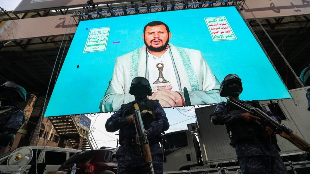 Members of Yemen’s security forces stand guard in front of a giant screen broadcasting the speech of Houthi leader Abdul-Malik al-Houthi in Sanaa, on July 6, 2025.