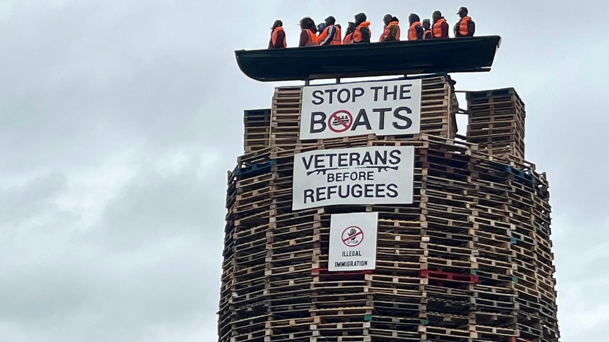 Models depicting migrants wearing life jackets in a small boat alongside two banners reading 'Stop the boats' and 'Veterans before refugees' are displayed on top a bonfire in Moygashel, Northern Ireland, on July 9, 2025.