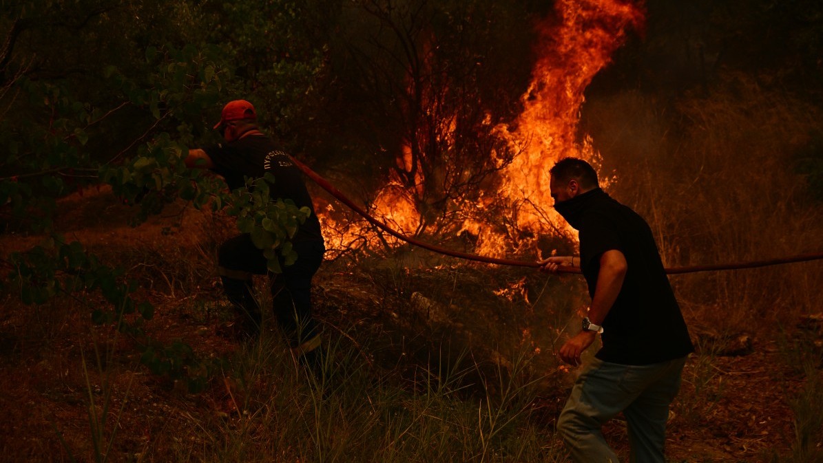 A firefighter (L) and a resident work to extinguish a wildfire near the city of Patras in western Greece on August 13, 2025.