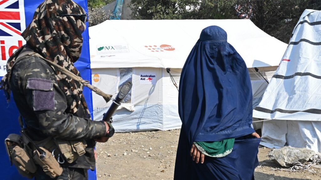 A Taliban security personnel stands guard as an Afghan burqa-clad woman walks past a mobile health clinic in the aftermath of an earthquake at Mazar Dara village in Nurgal district, Kunar province on September 14, 2025.