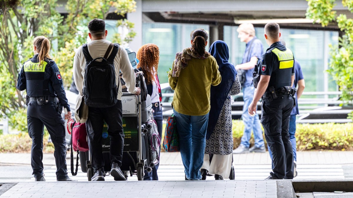 Afghan nationals walk past German policemen to board a bus after they landed at the airport in Hannover-Langenhagen, northwestern Germany, on September 1, 2025.