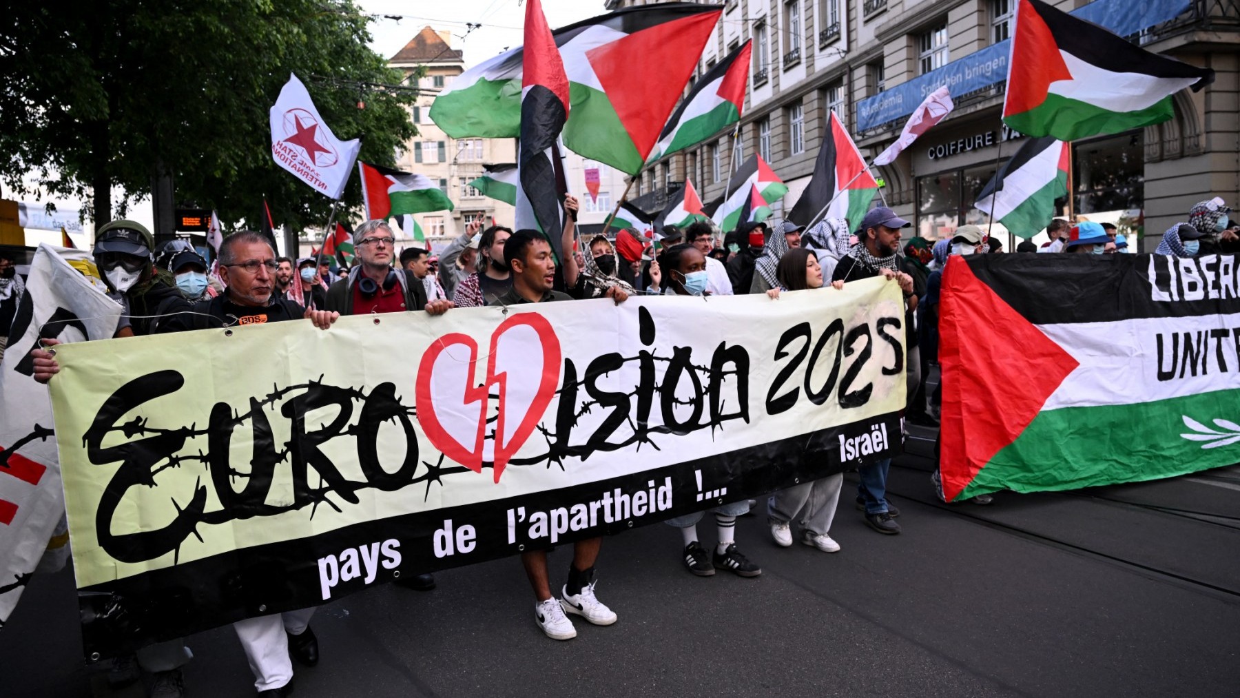 BDS (Boycott, Divest, Sanction) activists hold Palestinian flags and a banner reading "Country of apartheid ... Israel" during a demonstration against Israel's candidate prior to the grand final of the Eurovision Song Contest 2025 in Basel on May 17, 2025.