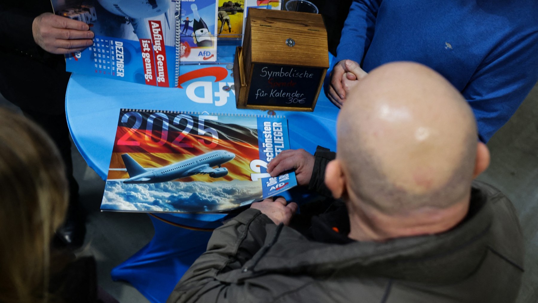 A supporter of Alice Weidel, co-leader of Germany's far-right Alternative for Germany (AfD) party, buys a calander of the ’12 most beautiful deportation airplanes’ as he waits for her to address an election campaign rally on January 25, 2025 in Halle, Germany.