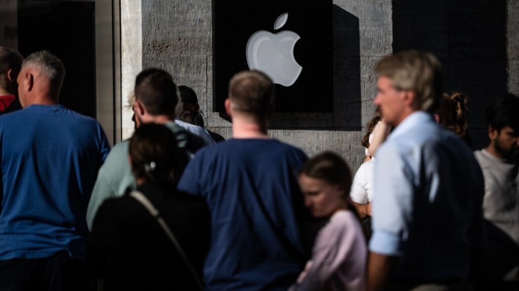 Customers queue up in front of a retail outlet of U.S. technology giant Apple, whose logo is seen on the wall in Berlin on September 19, 2025, as the company's iPhone 17 was released.