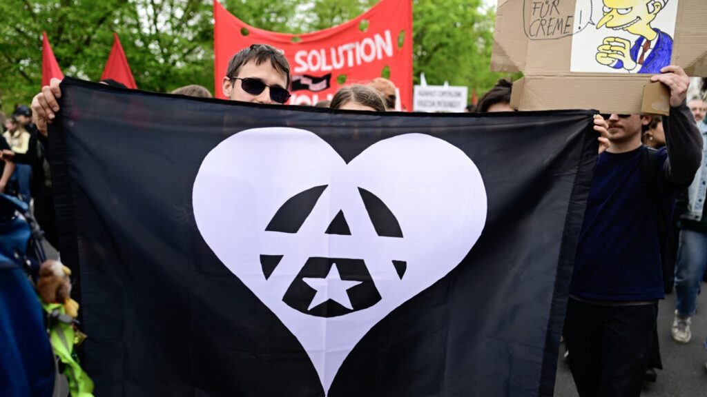 Protesters hold a black flag with anarchist symbols ‘Circle-A’ and a star in a white heart during the Revolutionary May Day demonstration in Berlin on May 1, 2023.