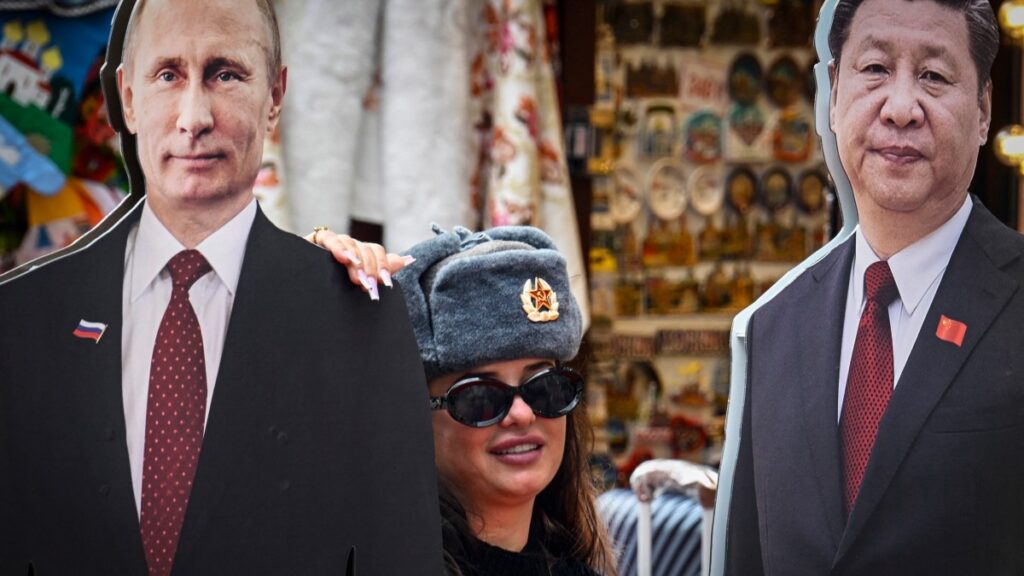 A tourist wearing a Soviet Army hat poses with cardboard images depicting Russian President Vladimir Putin and his Chinese counterpart Xi Jinping in central Moscow on June 24, 2025.