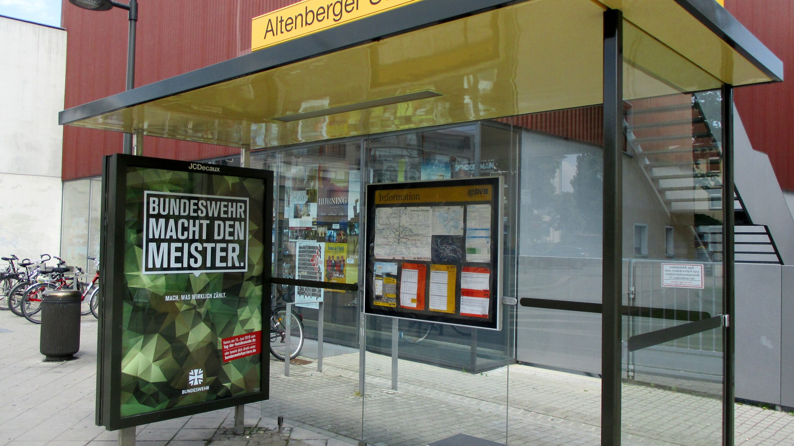 An ad on the plexiglass wall of a Dresden bus stop shelter says "The Bundeswehr Makes the Champion" in 2019.