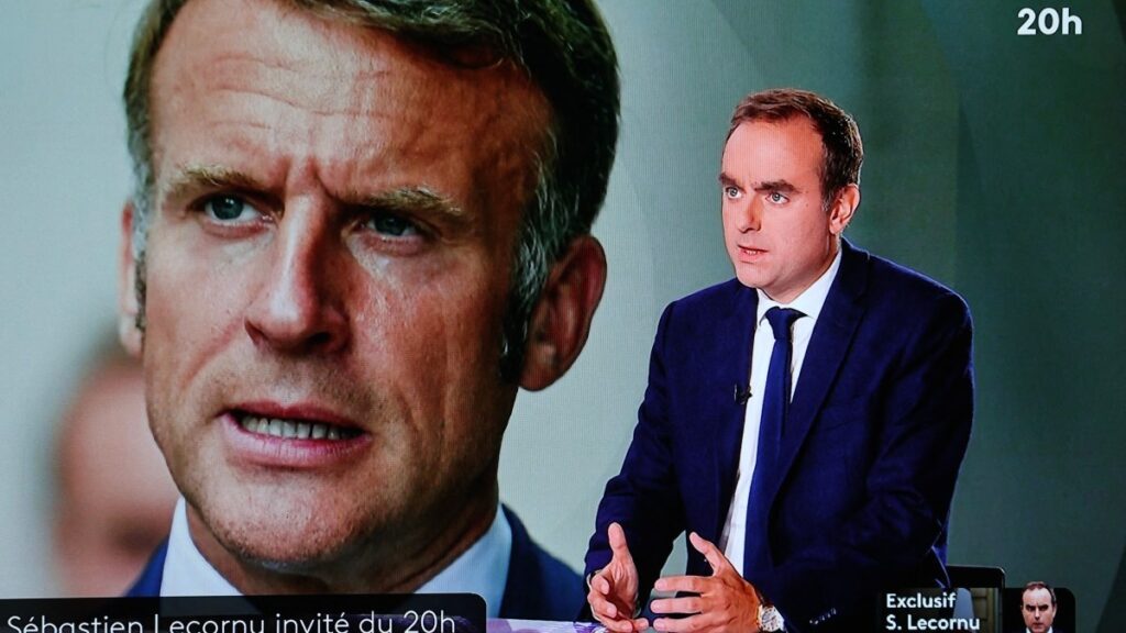 A television screen displaying France’s outgoing Prime Minister Sebastien Lecornu (R), with an image of Emmanuel Macron in the background, during a live broadcast interview with French TV France 2 on October 8, 2025.