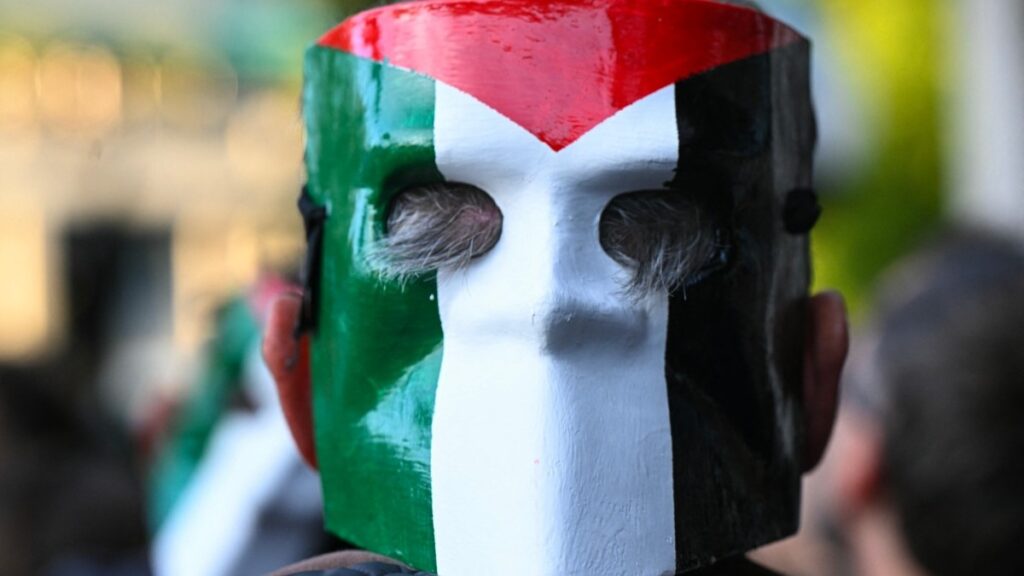 A pro-Palestinian protester wears a mask backwards depicting the Palestinian national flag as he gathers in solidarity with Palestine, on the eve of the match between Italy and Israel for the FIFA World Cup 2026 qualifiers, in Udine northeastern Italy, on October 14, 2025.