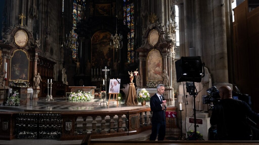 A crew of Austrian state television ORF report in front of a photo of Pope Francis on display in St. Stephen’s Cathedral in Vienna on April 21, 2025.