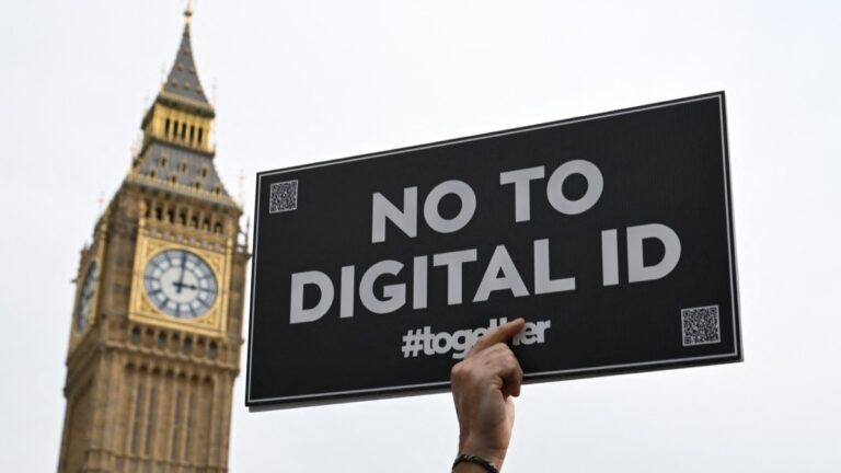 A demonstrator holds up a placard outside The Palace of Westminster during a march against the implementation of digital ID cards, in central London on October 18, 2025.