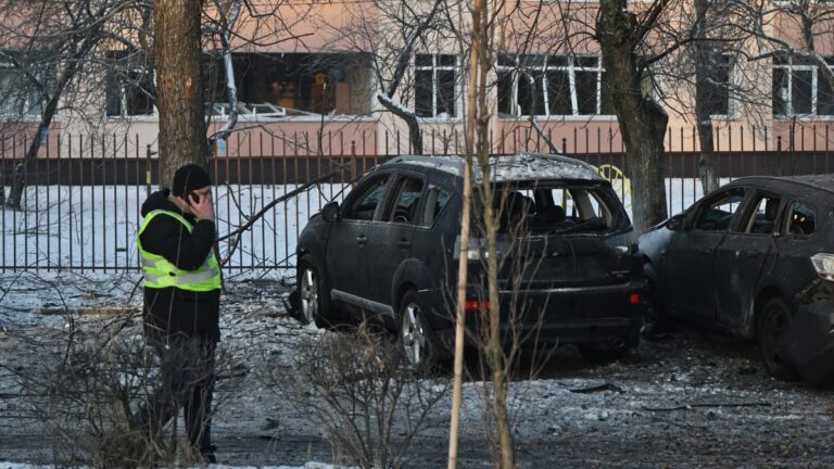 A policeman walks past damaged cars in front of a school with broken windows at the site where Russian drone debris fell during a large-scale Russian aerial attack in Kyiv on January 20, 2026.